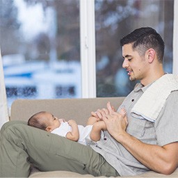 man sitting on a sofa looking down at baby lying on his legs.jpg