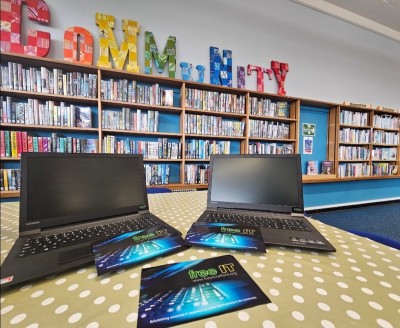 Two laptops on a table in a library. Free IT leaflets rest on the laptops.